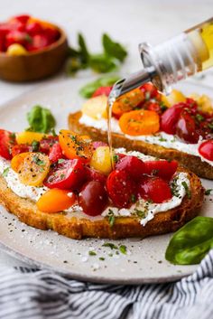 someone is pouring olive oil on some bread with tomatoes and other vegetables in the background