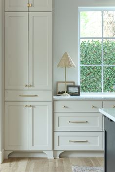 an empty kitchen with white cabinets and wood flooring in front of a large window