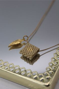 two pieces of jewelry sitting on top of a white table next to a gold frame