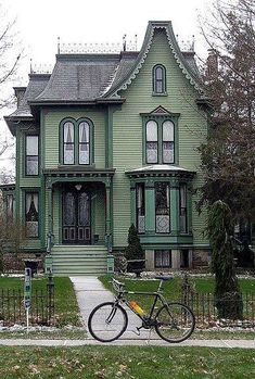 a bicycle is parked in front of a green victorian style house on a street corner