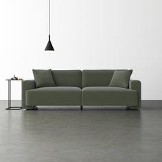 a green couch sitting on top of a gray floor next to a table with a lamp hanging from it