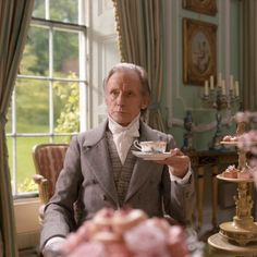 an old man sitting at a table with a cup and saucer in his hand