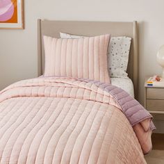 a bed with pink comforter and pillows on top of it next to a night stand