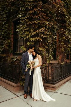 a bride and groom standing in front of an ivy covered building