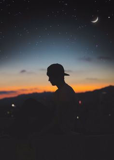 a man sitting on top of a hill under a night sky