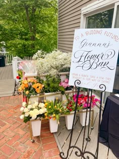 a sign that is on top of a stand with some flowers in front of it