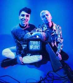 two young men sitting next to each other on top of a blue background with wires