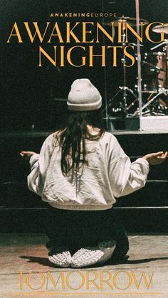 a person sitting on the ground in front of a stage with their arms spread out