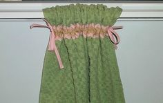 a green towel hanging on the side of a window sill with pink ribbon around it