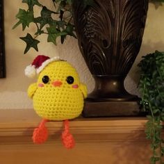 a crocheted yellow bird with a santa hat on it's head sitting next to a potted plant