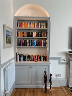 a bookshelf filled with lots of books on top of a wooden floor next to a white wall