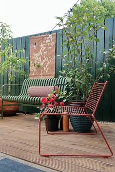 a chair and table on a wooden deck with potted plants in the foreground