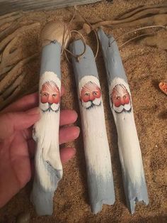 three painted wooden sticks with santa's faces on them, one being held by a hand