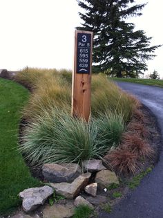 a wooden sign sitting on the side of a road next to a lush green field