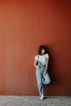 a woman leaning against a red wall with her hands in her pockets