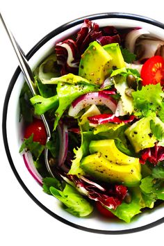 a salad with avocado, tomatoes and lettuce in a white bowl