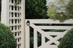 an open white gate surrounded by bushes and trees