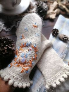 a knitted mitten with an embroidered crab and pine cone on it next to other items