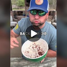 a man wearing sunglasses and a baseball cap is holding a bowl of food in front of his face