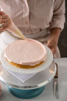 a woman is decorating a cake with pink frosting on it and holding a knife