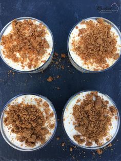 four desserts in small glass bowls with toppings on top, sitting on a blue surface