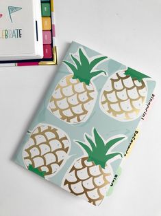 a notebook with pineapples on it next to some colored crayon pens