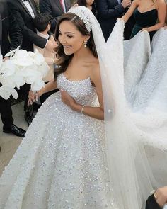 a woman in a white wedding gown and veil is walking through the crowd with other people