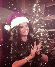 a woman wearing a santa hat standing in front of a christmas tree with her hands up