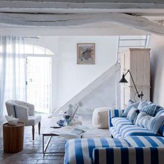 a living room with blue and white striped couches in front of a stair case