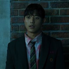 a young man wearing a suit and tie standing in front of a brick wall, looking at the camera