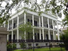 a large white house with many balconies on it's sides and black wrought iron fence