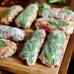 there are many rolls that have been wrapped in leafy wrappers on a cutting board