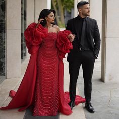 a man and woman in formal wear standing on the sidewalk next to each other wearing red dresses