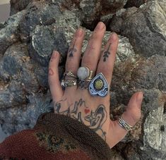 a person's hand with tattoos and rings on it next to large rock formation