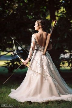 a woman in a wedding dress holding an arrow and bow with her back to the camera