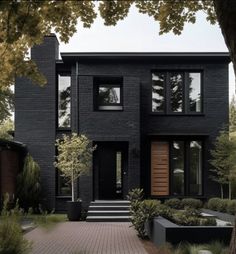 a black house with lots of windows and plants on the front yard, surrounded by trees