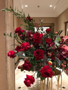 a vase filled with lots of red flowers on top of a table next to a mirror