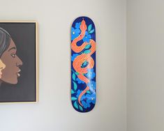 a blue skateboard hanging on the wall next to a painting and a woman's face