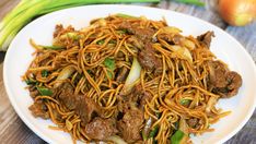 a white plate topped with meat and noodles on top of a wooden table next to green onions