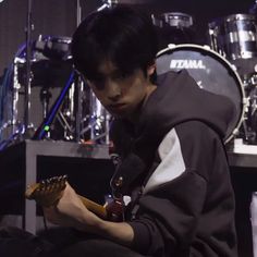 a young man sitting in front of a drum set and playing the guitar with his hands