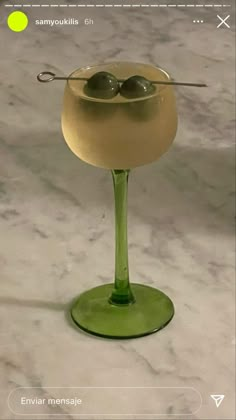 a green glass filled with liquid and two olives in it's beaker