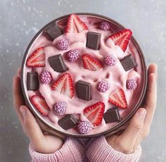 a person holding a bowl filled with fruit and chocolate