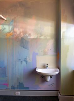 a white sink sitting next to a wall mounted faucet under a light fixture