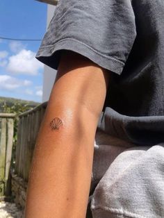 a person with a small shell tattoo on their left arm and the back of his arm