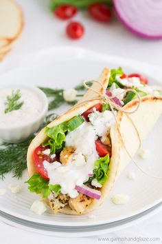 a chicken gyro with lettuce, tomatoes and onions on a white plate