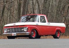 an old red and white truck parked on the side of the road in front of some trees