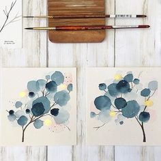 two paintings with blue flowers on them next to paintbrushes and watercolor pencils