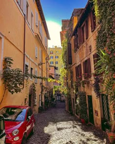 a red car parked on the side of a cobblestone street in an old town