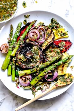 a white plate topped with asparagus and other veggies next to a bowl of sauce