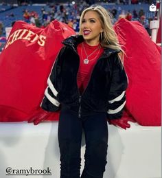 a woman sitting on top of a bench in front of a giant red pillow at a football game